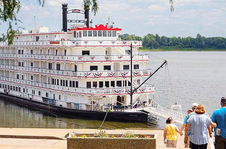 A paddlewheel riverboat docked on the Ohio River with guests walking on the landing